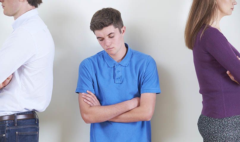 parents looking away from each other with sad teen boy in the middle