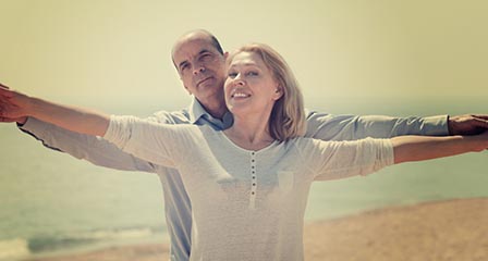 older couple on beach with arms outstretched