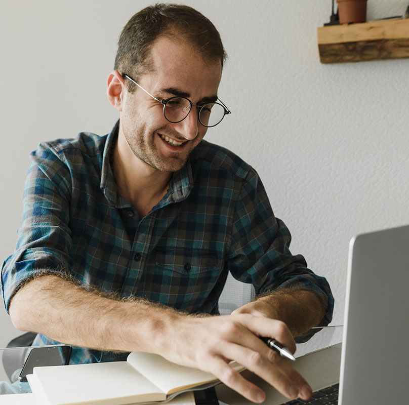 smiling man on laptop making notes