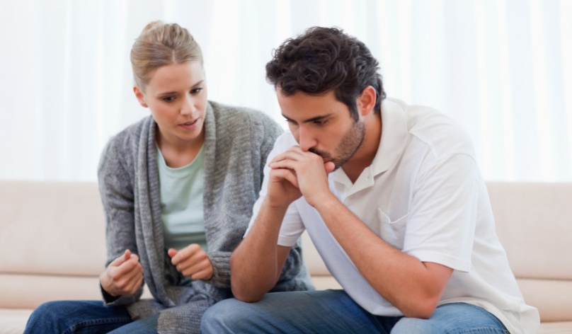 woman talking to worried male partner who is resting is chin in his hands
